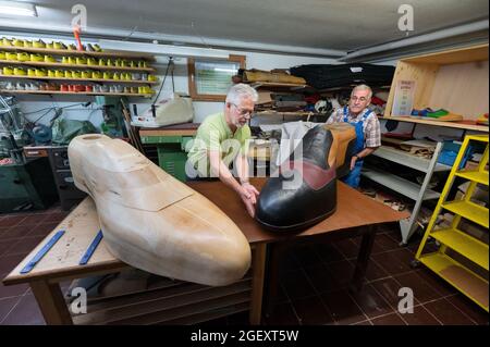 19. August 2021, Baden-Württemberg, Münsingen: Schuhmeister Matthäus Jörg (r) und Johannes Schunk drehen in Jörg's Werkstatt einen Riesenschuh. Jörg und Schunk haben den Schuh in der Größe 240 mit Hilfe eines Zimmermanns angefertigt. (To dpa 'Made in Münsingen - zwei Schuhmacher fertigen Schuhe in der Größe 240') Foto: Marijan Murat/dpa Stockfoto