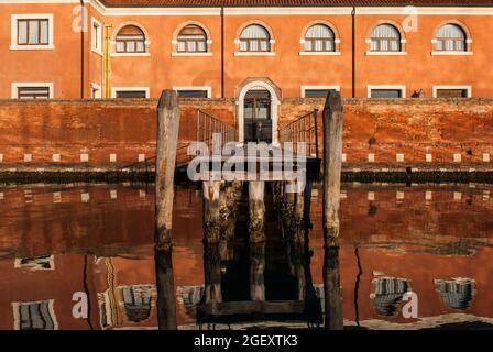 Ein Küstengebäude mit einer Brücke, die sich auf dem Wasser auf der Insel San Servolo in Venedig, Italien, widerspiegelt Stockfoto