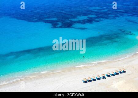 Die Reihen der Liegen mit Strohschirmen am Strand. Paradies am Strand und türkisfarbenem Meer. Sonniger Sommertag. Albanische riviera, Albanien, Europa Stockfoto
