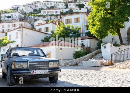 Alter Mercedes und Blick auf das Dorf Vuno - traditionelle weiße Häuser mit orangefarbenen Dächern und hölzernen Fensterläden, auf dem Berg, Albanien Stockfoto