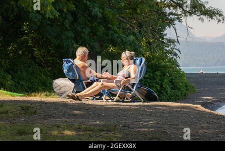 Ältere Paare genießen ihren Tag in Liegestühlen am Strand am Cultus Lake BC. Stockfoto