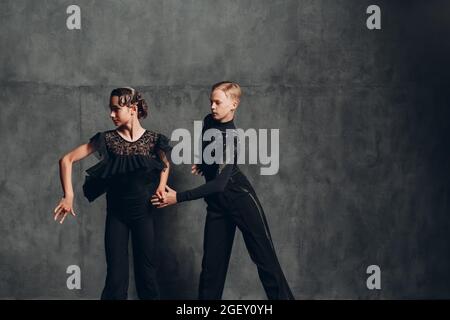 Junges Paar in schwarzem Kleid, das im Ballsaal tanzt. Zwei europäische professionelle Sporttänzer tanzen modernen zeitgenössischen Paartanz. Mann und Frau in Leidenschaft. Stockfoto