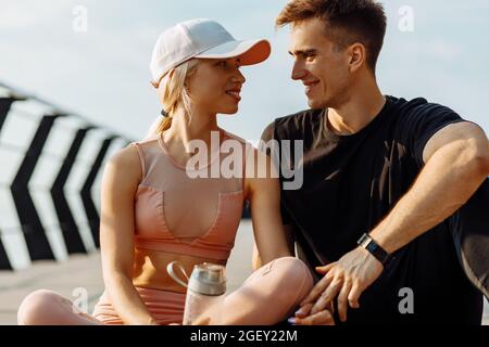 Gesundes Paar, das sich nach dem harten Training im Freien ausruhte, Paar, Mann und Frau, die sich nach dem Fitnesskurs auf der Fitnessmatte am Pier ausruhten Stockfoto