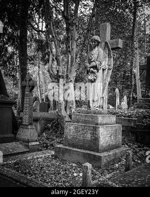 Eine vertikale Graustufenaufnahme eines Rauchgesteins auf dem Highgate-Friedhof in London mit einer Engelsstatue darauf Stockfoto