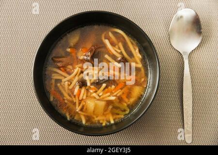 Suppe mit Nudeln und Pilzen in einer schwarzen Keramikschale und Löffel. Blick von oben Stockfoto