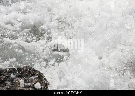 Spritzer von Meereswellen, die gegen Felsen krachen Stockfoto