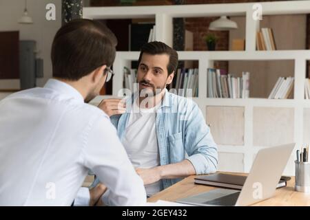 Geschäftsleute, männliche Angestellte, die sich unterhalten, sitzen am Schreibtisch Stockfoto