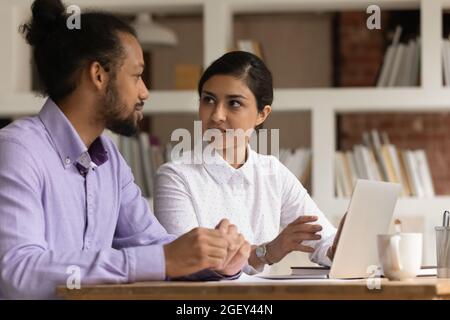 Zwei multiethnische Kollegen sitzen am Schreibtisch und diskutieren über aktuelle Geschäfte Stockfoto