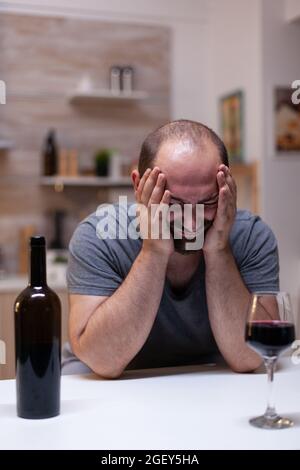 Depressiver Mann mit Alkoholismus sitzt mit Flasche und Glas Wein und trinkt und fühlt sich einsam. Gestresster Erwachsener mit Angst süchtig mit alkoholischem Getränk, Alkohol, Alkohol Stockfoto