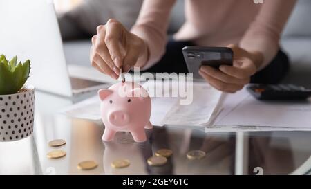 Nahaufnahme weibliche Hände halten Smartphone setzen Euro-Münze in Sparschwein Stockfoto