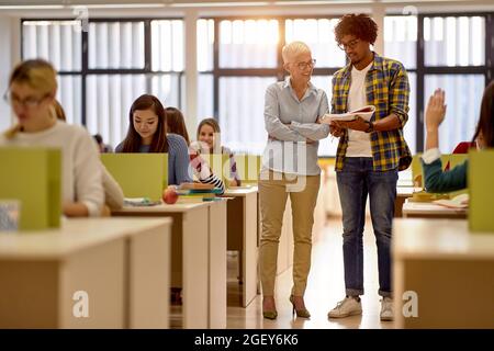 Ein männlicher Student im Klassenzimmer der Universität spricht mit einem Professor über neue Lektionen. Intelligente junge Menschen studieren an der Hochschule. Bildung, colle Stockfoto