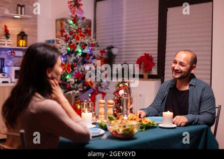 Glückliche Familie sitzt am romantischen Esstisch in Weihnachten dekoriert Küche genießen weihnachtsessen zusammen. Fröhliche Menschen genießen die Winterfeiertage und feiern weihnachten Stockfoto