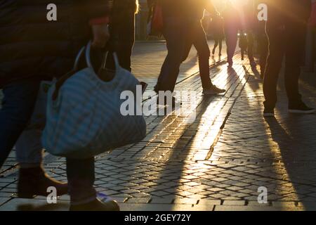 Silhouetten von Pendlern am Morgen mit Sonnenlicht, das während der Hauptverkehrszeit an einem belebten Bahnhof durch die Beine und Füße in Bewegung strahlt Stockfoto