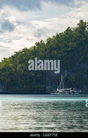 Friwin, Indonesien - 14. Okt 2019: Ein Touristenboot, ein Katamaran-Segelboot, fährt langsam entlang einer riesigen Insel, Raja Ampat, West Papua Stockfoto