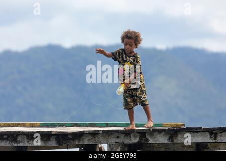 Friwin, Indonesien - 14. Okt 2019: Ein kleiner Junge spielt und versucht, etwas im Wasser von einem hölzernen Steg, Raja Ampat, West Papua, zu fischen Stockfoto