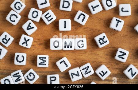 Kleine weiße und schwarze Perlenwürfel auf Holzbrett, Buchstaben in der Mitte buchstabieren OMG. Stockfoto