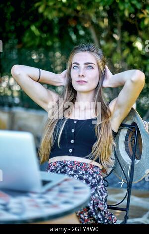 Porträt einer jungen kaukasischen Frau, die mit einem Laptop im Garten posiert und im Internet nach Informationen sucht. Lifestyle-Konzept. Stockfoto