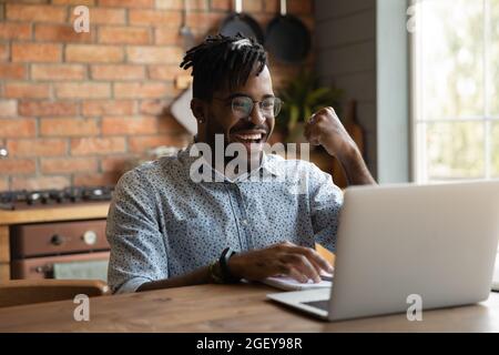 Aufgeregt afrikanischen Millennial Kerl mit Laptop zu Hause Stockfoto