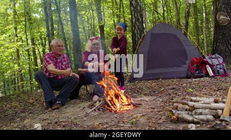 Großvater der älteren Großmutter mit Enkelin, die Würstchen über dem Lagerfeuer in Holz braten Stockfoto