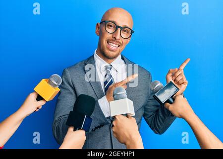 Kahlköpfiger Mann mit Bart, der von Reportern interviewt wurde, die die Mikrofone lächelnd hielten und die Kamera mit zwei Händen und Fingern auf die si zeigten Stockfoto