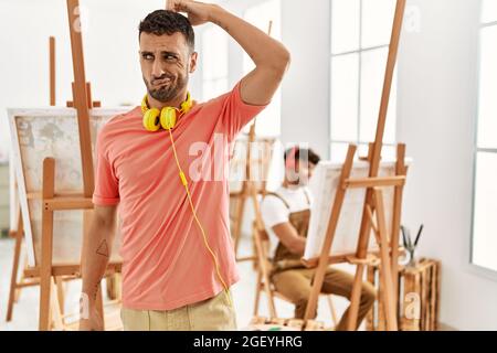 Junger hispanischer Mann im Kunststudio verwirrt und wundert sich über Fragen. Unsicher mit Zweifel, Denken mit Hand auf Kopf. Nachdenkliches Konzept. Stockfoto