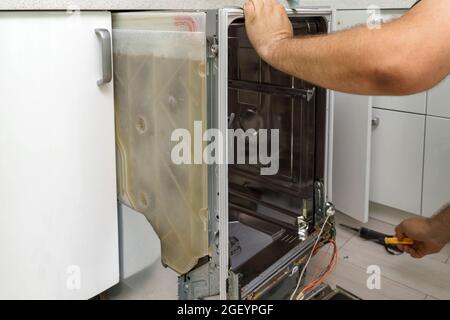 Reparieren eines Hausspülers. Der Master zieht den eingebauten Geschirrspüler zur Reparatur heraus Stockfoto