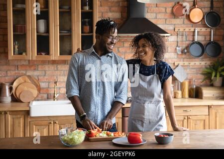 Glückliches süßes afroamerikanisches Paar, das frischen Salat kocht Stockfoto