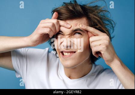 Kerl in weißem T-Shirt quetscht Pickel auf seinem Gesicht Teenager Stockfoto