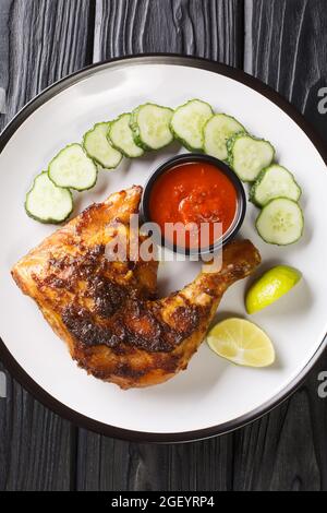 Ayam bakar ist ein indonesisches und malaysisches Gericht, das aus kohlegrillierten Hähnchen besteht, serviert mit Gurke und heißer Sauce in der Nähe auf dem Teller Stockfoto