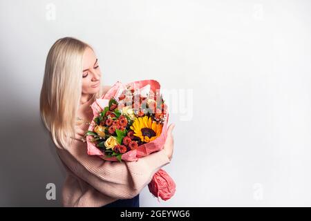 Die junge Frau lächelt und hält einen großen und schönen Herbststrauß mit Sonnenblumen, Chrysanthemen und Rosen, mit Kopierraum Stockfoto