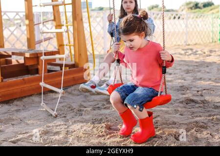 Kinder haben Spaß auf Holzspielplatz im Freien, zwei kleine Mädchen spielen draußen, tun verschiedene gesunde Aktivitäten an sonnigen Tag, Kinder Kletterwand Stockfoto