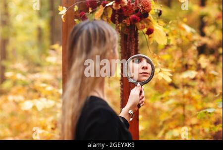 Szenische Foto von jungen schönen Mädchen mit Abend Make-up trägt schwarze Hexe Kostüm halten Spiegel und Blick auf sie während halloween Fotosession i Stockfoto