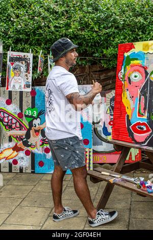 Junger männlicher Künstler, der sein Gemälde auf Leinwand fertig gestellt hat und in einem Garten steht. Stockfoto