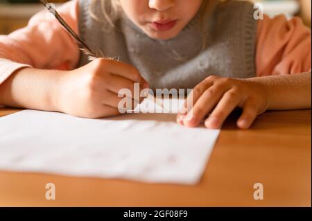 Das kleine siebenjährige Mädchen zeichnet eine verschwindende Zeichnung auf ein Papier mit einem echten geschärften Entenschreiber, der Milch anstelle von Tinte verwendet Stockfoto