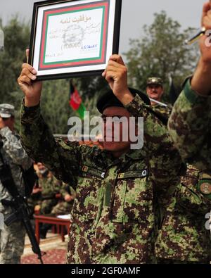 Der KABUL-afghanische National Army-Privatperson Mohammed Khalil, der 100.000ste Absolvent des Basic Warrior Training, der ein Alphabetisierungstraining absolviert hat, erhält von Brig eine Plakette und einen Stift. General Amlaqullah Patyani, Kommandant des Militärausbildungszentrums von Kabul, im Militärausbildungszentrum von Kabul in Kabul, Afghanistan, 28. Juli 2011, in Anerkennung der Leistungen der afghanischen Nationalen Sicherheitskräfte im Bereich Bildung und Alphabetisierung. Grundlegende Kriegerausbildung Kandak 162 absolvierte 1,287 Soldaten, die alle an verschiedenen Zweigschulen der afghanischen Nationalarmee oder dem Consolidated Fielding Center weiterbilden werden Stockfoto