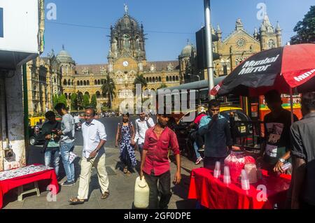 Mumbai, Maharashtra, Indien : die Menschen gehen an einem Stand für kalte Getränke vor dem UNESCO-Weltkulturerbe Chhatrapati Shivaji Terminus Bahnhof (früher Stockfoto