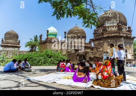 Bijapur, Karnataka, Indien : Pilger sitzen außerhalb des zweifachen Pilgerortes Jod Gumbad aus dem 17. Jahrhundert. Stockfoto