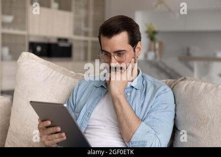Fokussierter Millennials-Mann mit Brille, Tablet-PC, E-Mail-Nachricht lesen Stockfoto