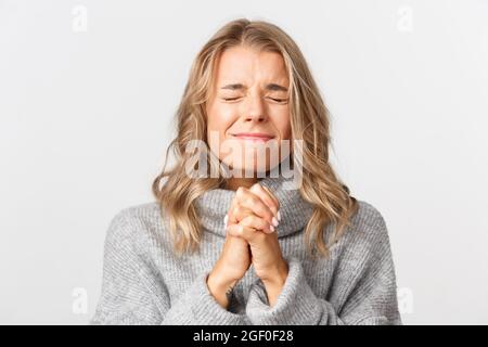 Close-up von hoffnungsvollen blonde Mädchen warten auf Chance, schließen Augen und zusammenklammernden Händen, flehend, stehend über weißem Hintergrund Stockfoto