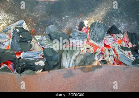 Glühende Kohlen schwelen in einem alten Metallgrill. Stockfoto