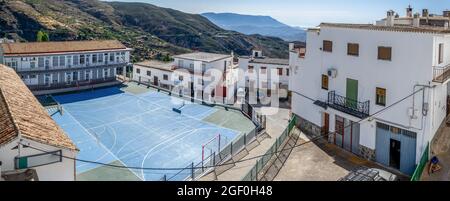 Panorama des Sportplatzes in der Schule von Mecina Bombaron in La Alpujarra von oben gesehen, umgeben von Bergen und weißen Häusern, mit Basketball-h Stockfoto