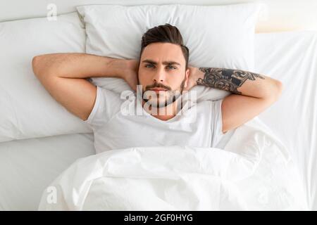 Deprimierter junger Mann, der nicht schlafen konnte, im Bett lag, aufblickte und nachdachte, Draufsicht Stockfoto