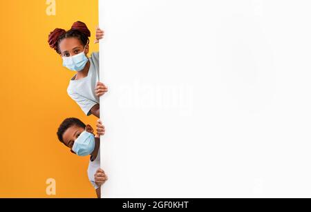 Schwarzer Bruder, Schwester in Gesichtsmasken, die neben leerem Brett steht Stockfoto