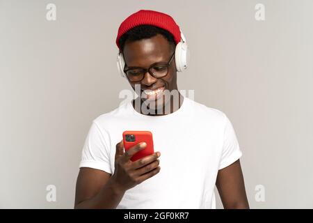 Schwarzer Mann hört Musik in kabellosen Kopfhörern über soziale Medien auf dem Smartphone. Studioaufnahme. Stockfoto