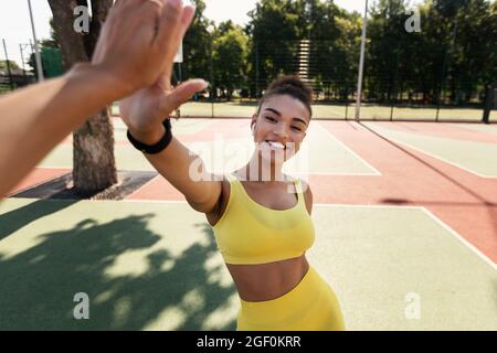 Sportliche schwarze Frau in gelber Sportbekleidung, die hohe fünf gibt Stockfoto