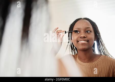 Porträt einer jungen afroamerikanischen Frau, die morgens Mascara aufsetzt, während sie sich schminkt und den Spiegel und den Kopierraum anschaut Stockfoto