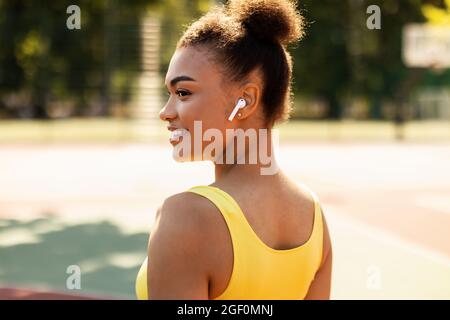 Sportliche schwarze Frau in gelber Sportkleidung, die Musik hört Stockfoto