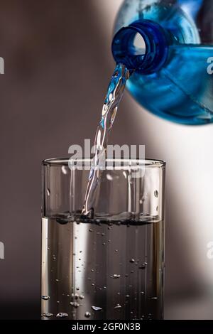 Ein Mann gießt Wasser aus einer Plastikflasche in ein Glas auf unscharfem Hintergrund Stockfoto