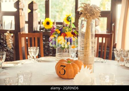 Festliche Floristik im Herbststil mit Nummerierung von Tischen auf Kürbissen im Bankettsaal. Floristik und Dekoration von Veranstaltungen Blumenarrangements. Stockfoto