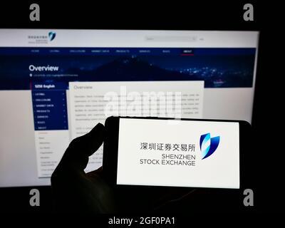 Person, die das Smartphone mit dem Logo der chinesischen Shenzhen Stock Exchange (SZSE) auf dem Bildschirm vor der Website hält. Konzentrieren Sie sich auf die Telefonanzeige. Stockfoto